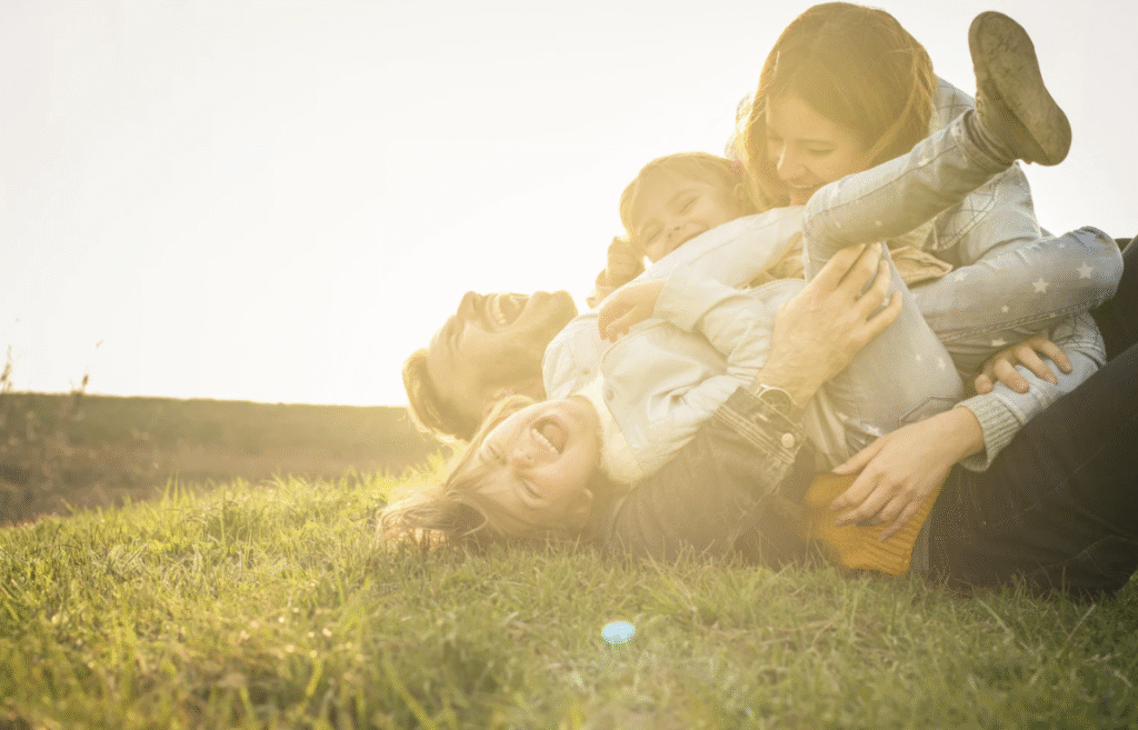 Two parents with children play fight on the grass with a sunny background